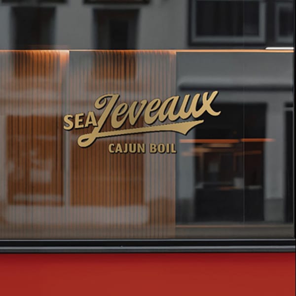 Golden "Sea Jeveaux Cajun Boil" logo on a frosted glass window with a red base.