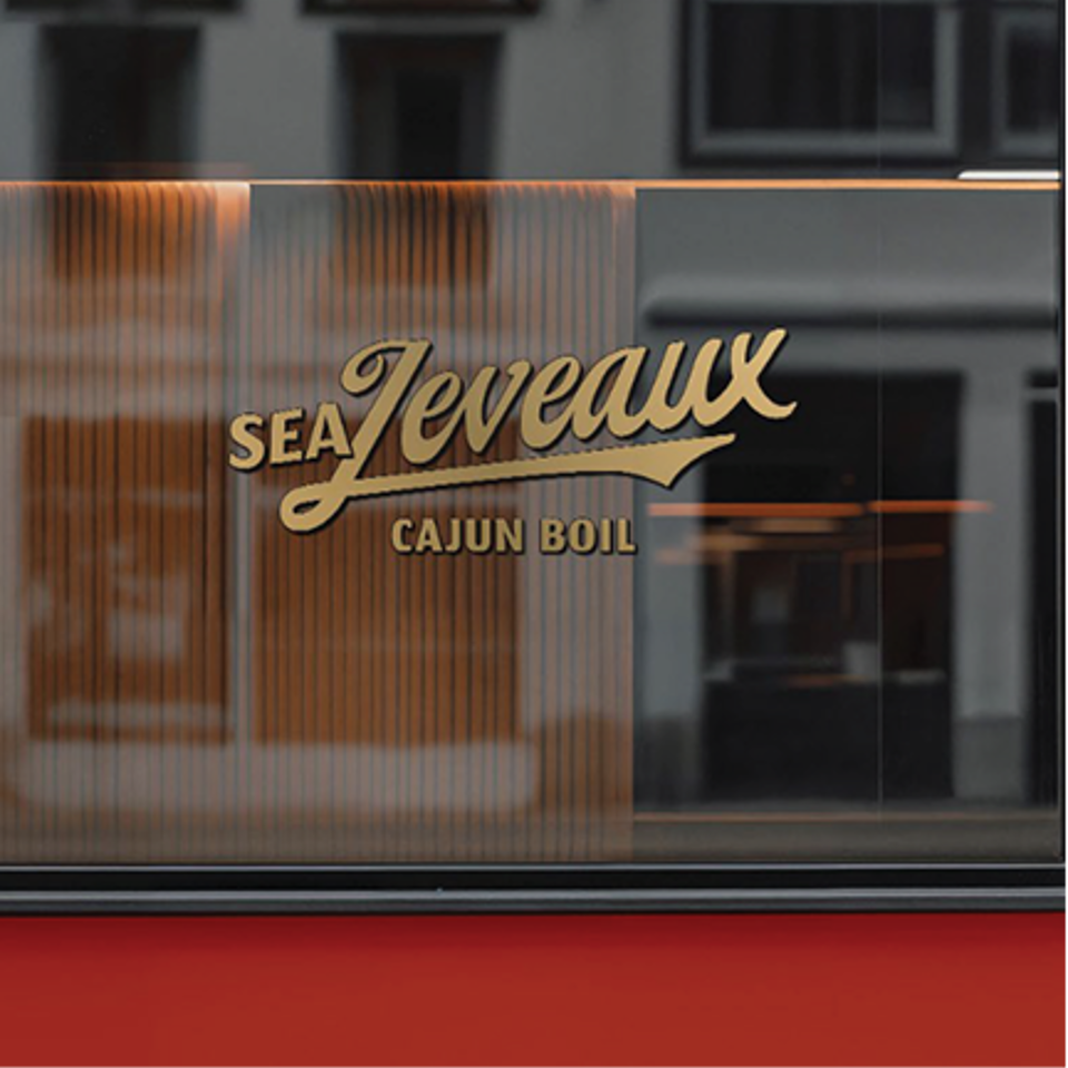 Golden "Sea Jeveaux Cajun Boil" logo on a frosted glass window with a red base.
