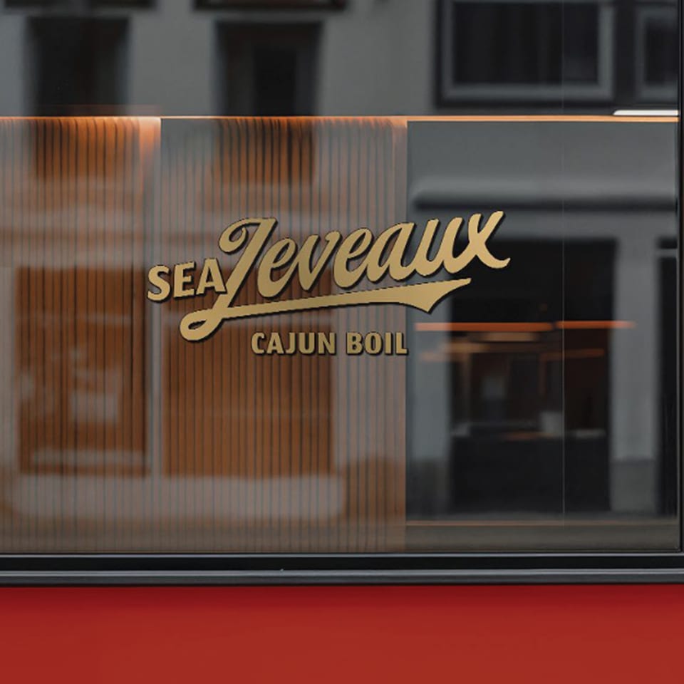Gold "Sea Jeveaux Cajun Boil" logo on a dark glass window with a red bottom.