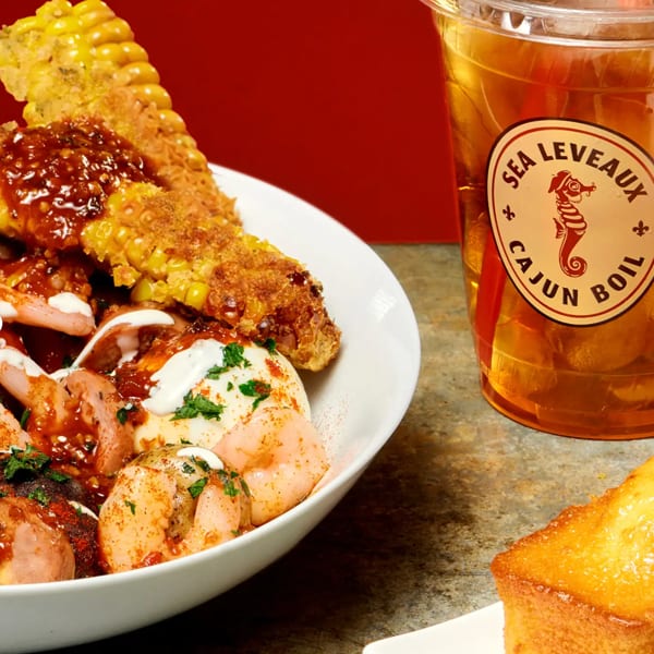 Cajun seafood boil with shrimp, sausage, corn, potatoes, and sauces beside a Sea Level Cajun Boil drink and cornbread.