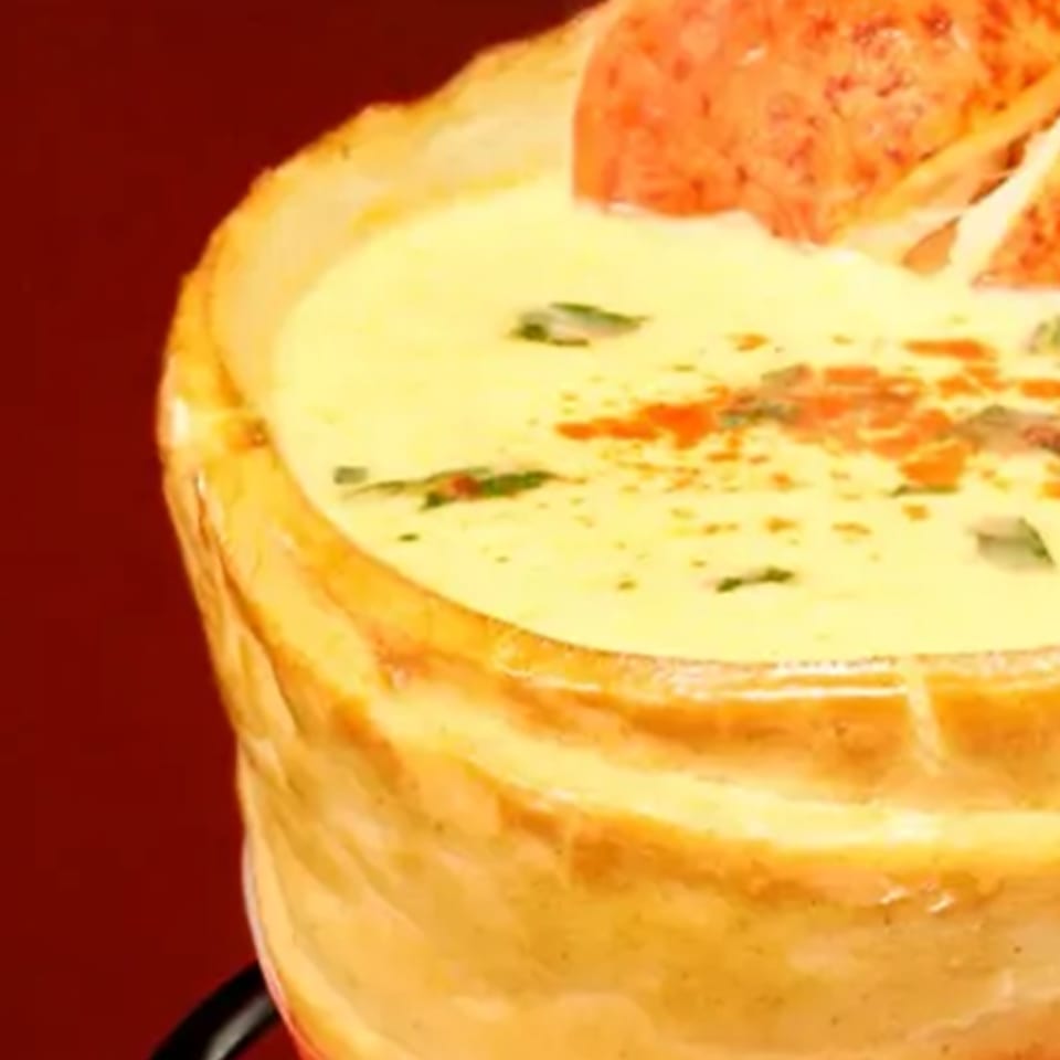 Creamy soup in a bread bowl, garnished with herbs and red pepper flakes.
